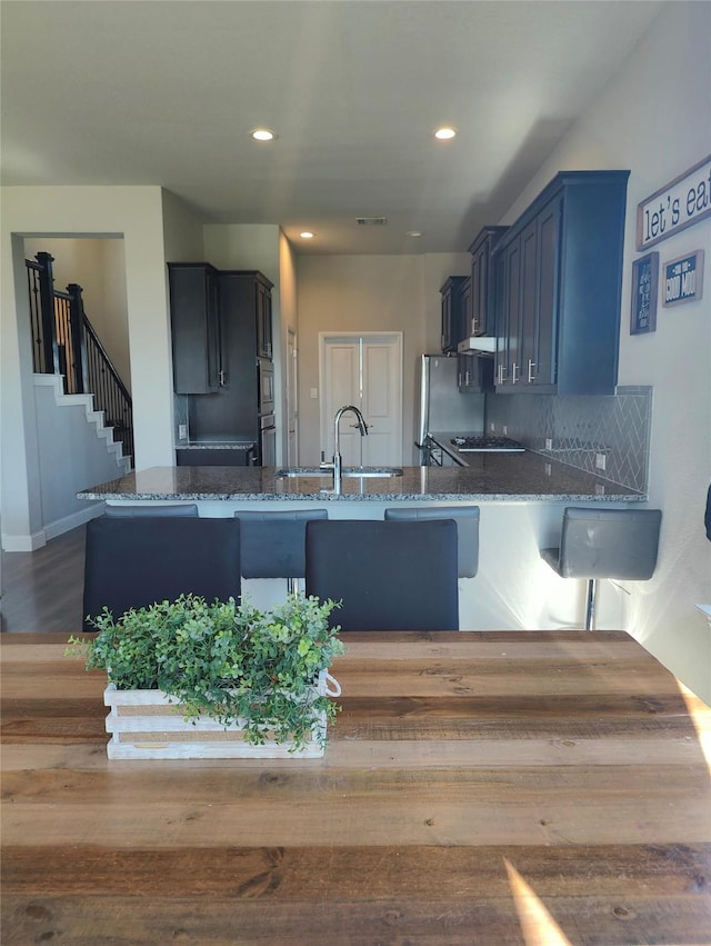 kitchen with backsplash, appliances with stainless steel finishes, a sink, dark stone countertops, and a peninsula