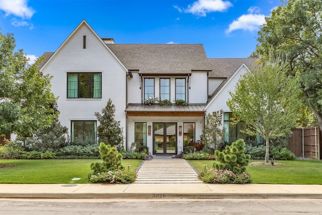 view of front of home featuring french doors, brick siding, a front lawn, and a standing seam roof