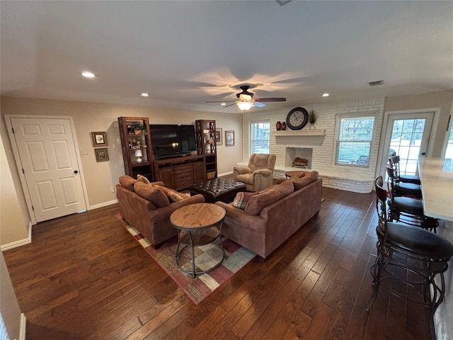 living room with a fireplace, ceiling fan, and dark wood-type flooring