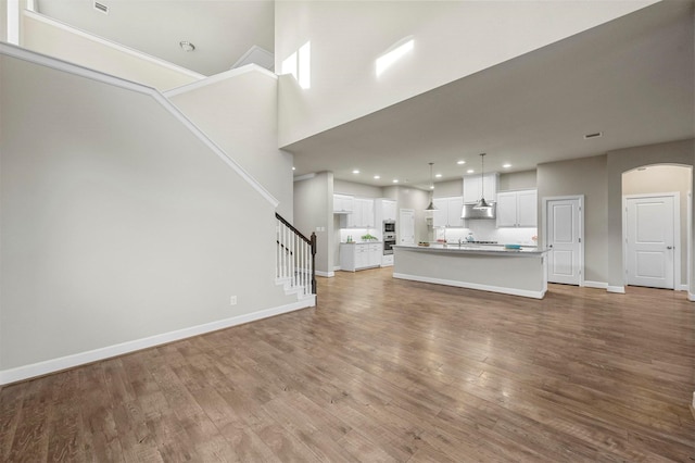 unfurnished living room with light wood-type flooring, recessed lighting, arched walkways, baseboards, and stairs