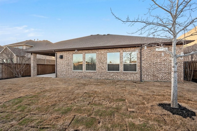 back of property featuring brick siding, a shingled roof, a yard, a fenced backyard, and a patio