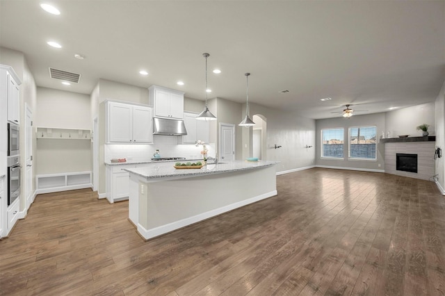 kitchen with visible vents, white cabinetry, hardwood / wood-style flooring, under cabinet range hood, and a glass covered fireplace