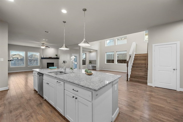 kitchen featuring stainless steel dishwasher, dark wood-style floors, open floor plan, white cabinetry, and a fireplace