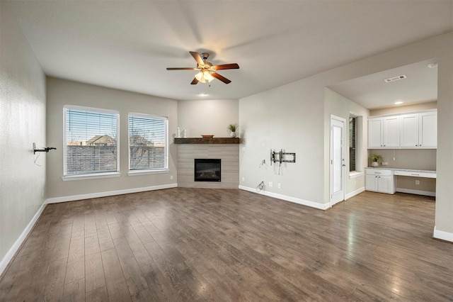 unfurnished living room with visible vents, dark wood-type flooring, ceiling fan, and a fireplace