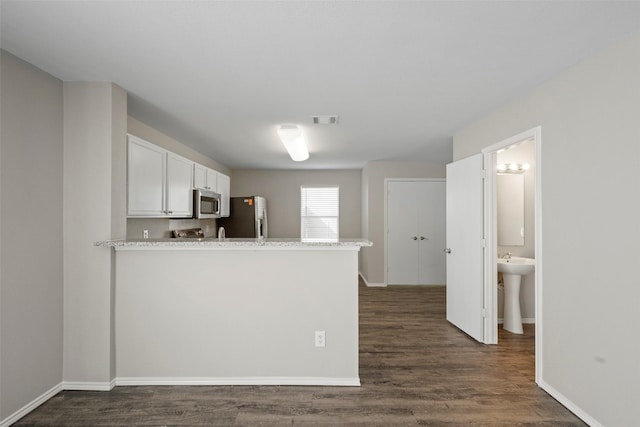 kitchen with appliances with stainless steel finishes, dark wood-type flooring, light stone counters, white cabinets, and kitchen peninsula