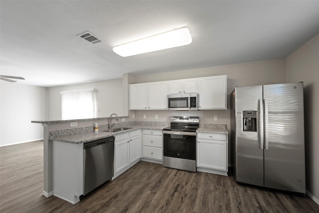 kitchen with kitchen peninsula, appliances with stainless steel finishes, white cabinets, and dark hardwood / wood-style flooring