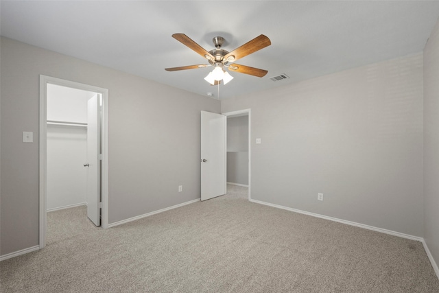 unfurnished bedroom featuring ceiling fan, light carpet, a walk in closet, and a closet