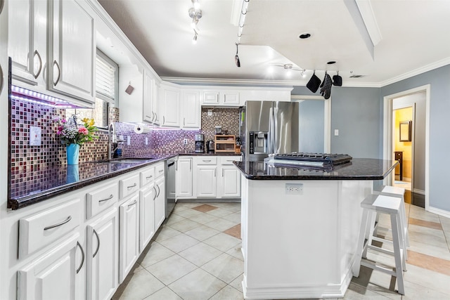 kitchen with appliances with stainless steel finishes, ornamental molding, a kitchen island, sink, and white cabinetry