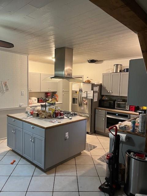 kitchen with light tile patterned floors, island exhaust hood, white cabinetry, stainless steel appliances, and wood ceiling