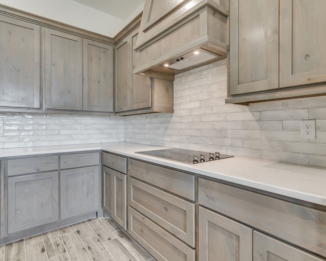 kitchen with backsplash, custom exhaust hood, black electric cooktop, and light stone countertops