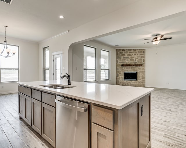 kitchen with sink, ornamental molding, pendant lighting, stainless steel dishwasher, and a kitchen island with sink