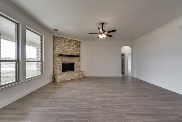 unfurnished living room with ceiling fan, ornamental molding, a stone fireplace, and light hardwood / wood-style floors