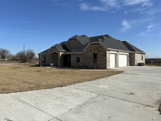 view of front of home featuring driveway, stone siding, roof with shingles, an attached garage, and brick siding