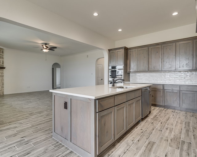 kitchen with an island with sink, sink, backsplash, stainless steel dishwasher, and ceiling fan