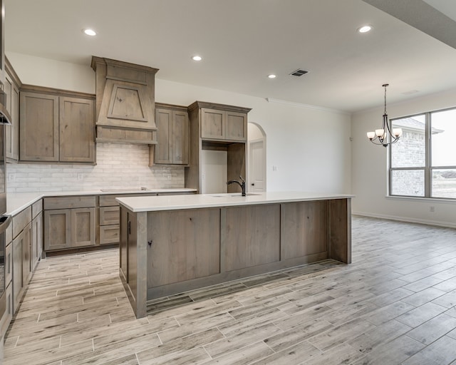 kitchen featuring stovetop, sink, backsplash, custom range hood, and an island with sink