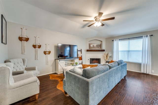 living area with a fireplace, a ceiling fan, baseboards, vaulted ceiling, and dark wood finished floors