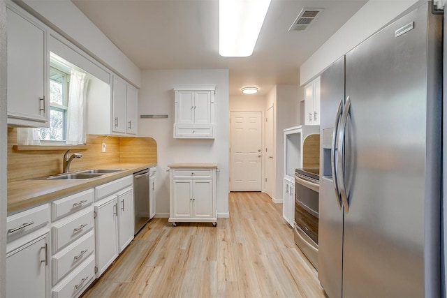 kitchen featuring stainless steel appliances, a sink, visible vents, white cabinetry, and light countertops
