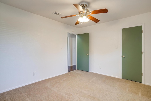 spare room with a ceiling fan, light colored carpet, visible vents, and baseboards