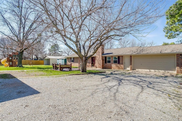 view of front of house featuring gravel driveway, brick siding, a playground, an attached garage, and a front lawn