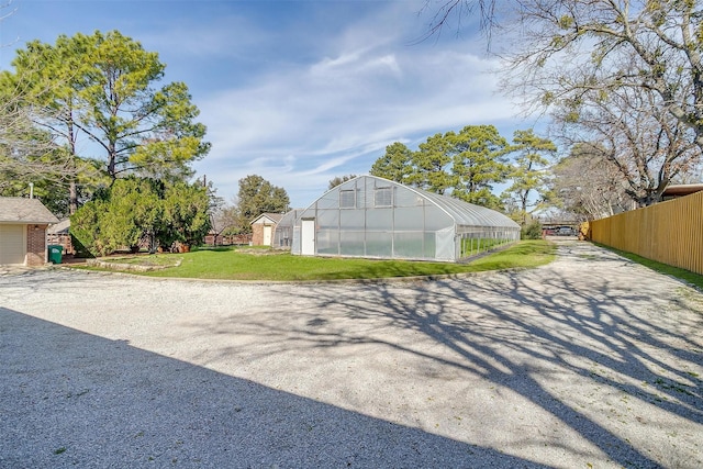 view of greenhouse featuring fence and a lawn