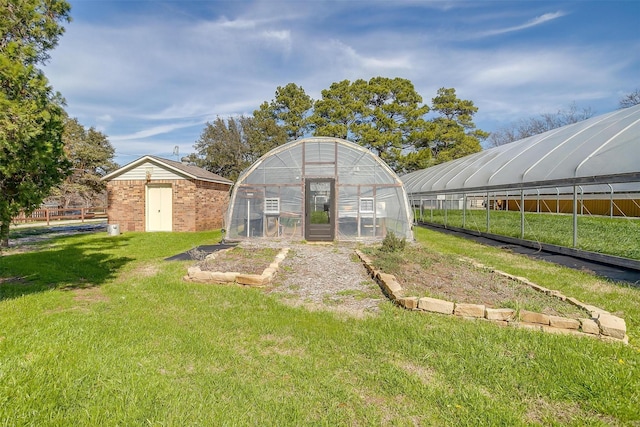 back of property featuring a greenhouse, brick siding, an outdoor structure, and a lawn
