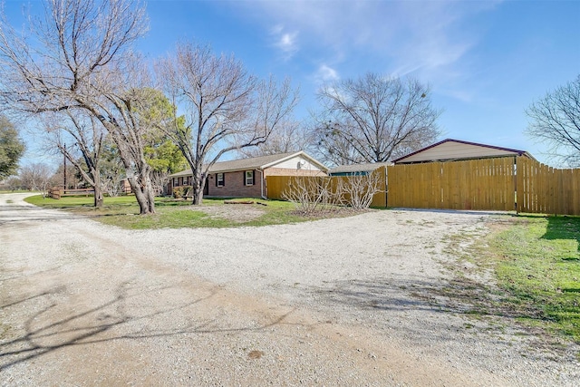 view of front facade featuring dirt driveway, fence, and brick siding