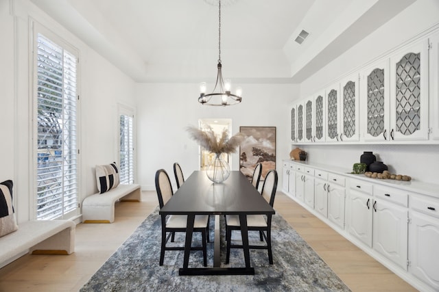 dining space with a raised ceiling, light wood-type flooring, and an inviting chandelier