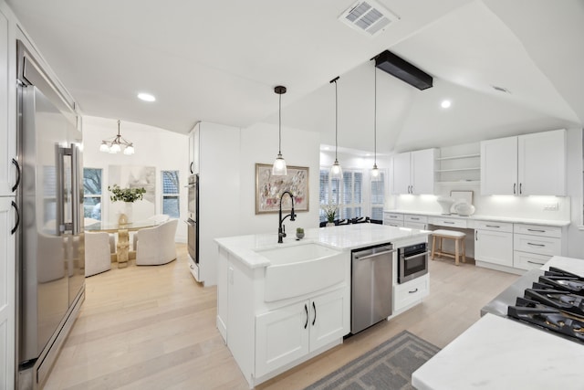 kitchen featuring an island with sink, decorative light fixtures, sink, appliances with stainless steel finishes, and white cabinets