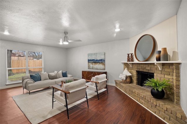 living area featuring a ceiling fan, a fireplace, a textured ceiling, and wood finished floors