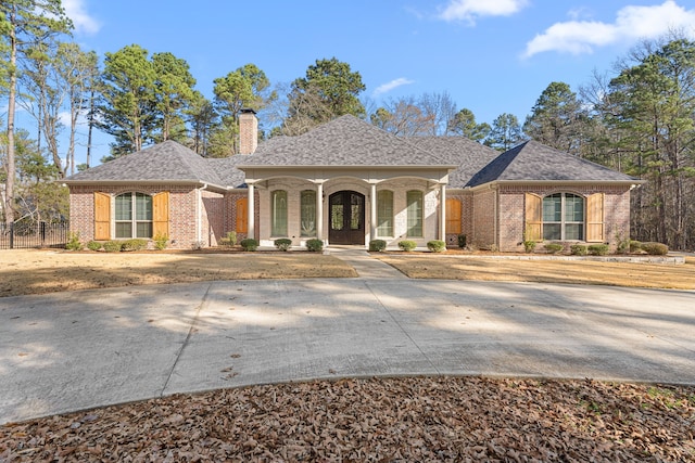 view of front of home featuring a porch, brick siding, a shingled roof, and a chimney