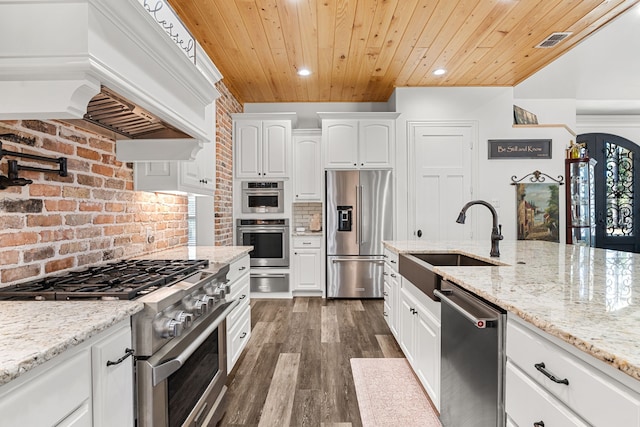 kitchen with premium appliances, light stone counters, white cabinets, a sink, and premium range hood