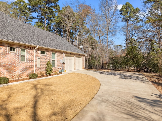 view of side of home featuring driveway, roof with shingles, a garage, and brick siding