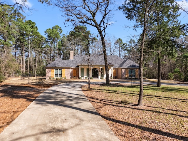 view of front of home with concrete driveway, brick siding, a chimney, and a front lawn