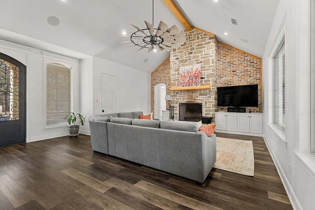 living area featuring vaulted ceiling with beams, a stone fireplace, dark wood-type flooring, and visible vents