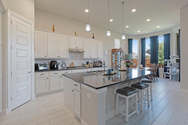 4024 Rosin St, Aubrey, TX 76227 - kitchen featuring tasteful backsplash, stainless steel gas stovetop, an island with sink, white cabinets, and under cabinet range hood