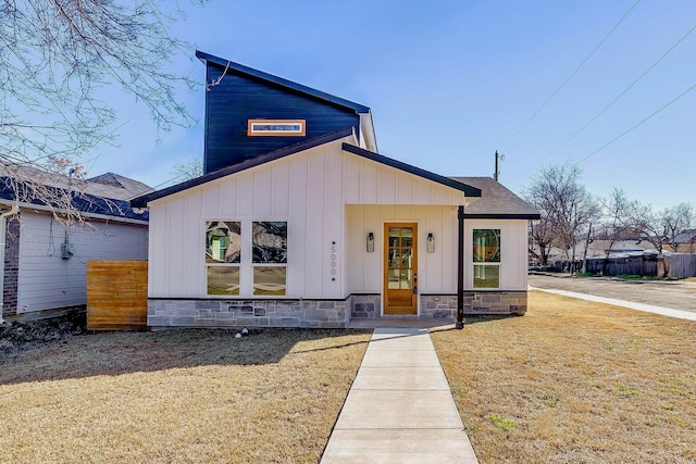 view of front of home featuring stone siding, a shingled roof, a front lawn, and board and batten siding