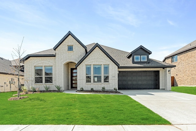 french country style house with concrete driveway, roof with shingles, a front lawn, brick siding, and a garage