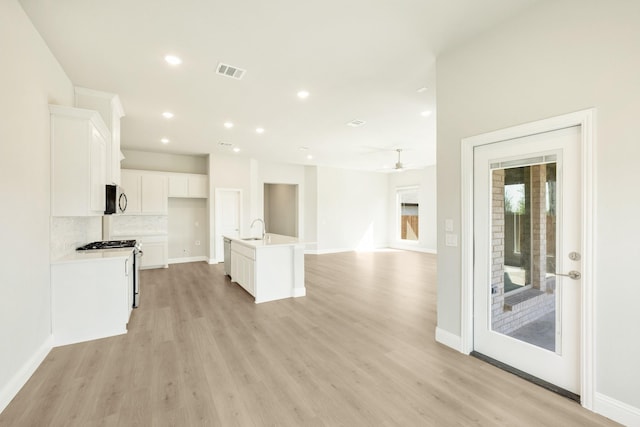 unfurnished living room with light wood-style floors, ceiling fan, visible vents, a sink, and baseboards