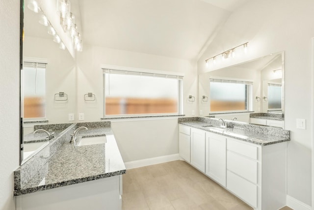 full bath featuring two vanities, baseboards, a sink, and lofted ceiling