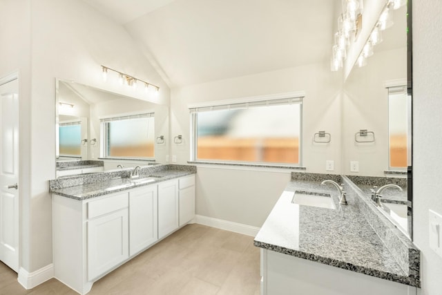 bathroom with baseboards, two vanities, a sink, and lofted ceiling