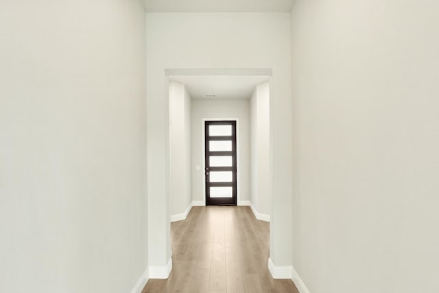 corridor featuring baseboards and light wood finished floors
