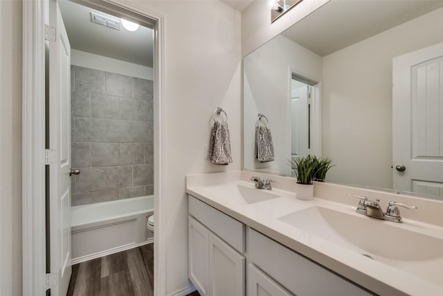 full bathroom with wood-type flooring, vanity, tiled shower / bath combo, and toilet