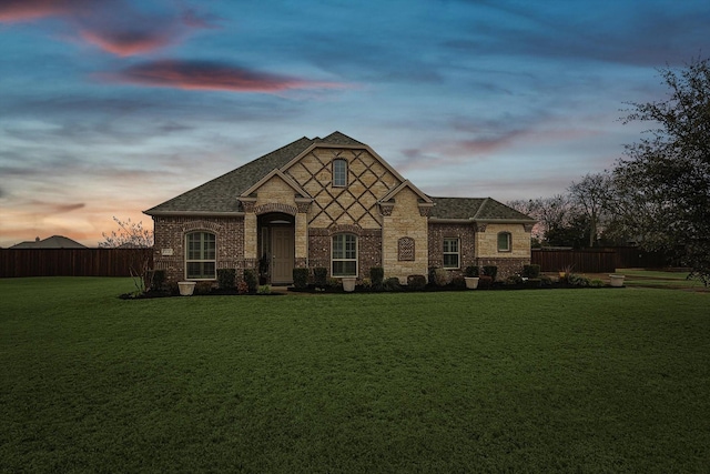 french country home featuring brick siding, roof with shingles, fence, and a yard