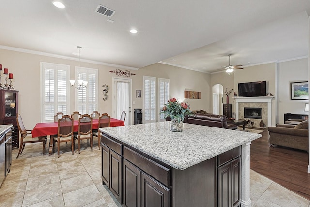 kitchen featuring decorative light fixtures, a tiled fireplace, ornamental molding, a kitchen island, and dark brown cabinets