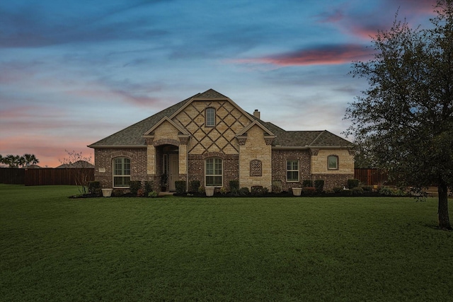 french provincial home featuring brick siding, a chimney, fence, and a yard