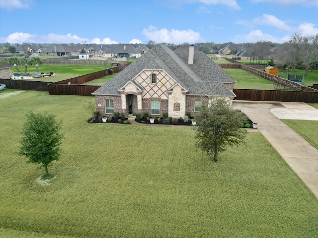 french country inspired facade with a shingled roof, a chimney, fence, and a front yard