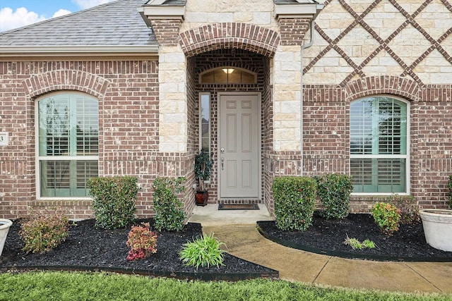 property entrance with a shingled roof and brick siding