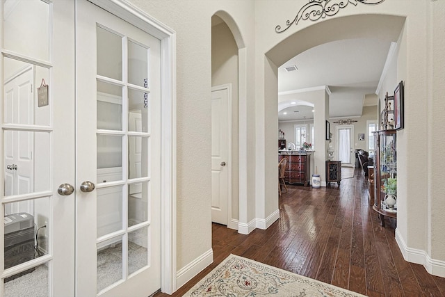 hall with baseboards, visible vents, arched walkways, dark wood-style floors, and ornamental molding