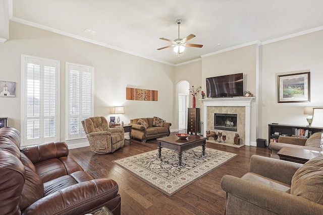 living room with arched walkways, a tile fireplace, baseboards, dark wood finished floors, and crown molding