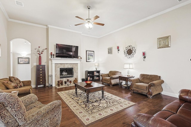 living area with visible vents, arched walkways, a tile fireplace, dark wood-style flooring, and crown molding